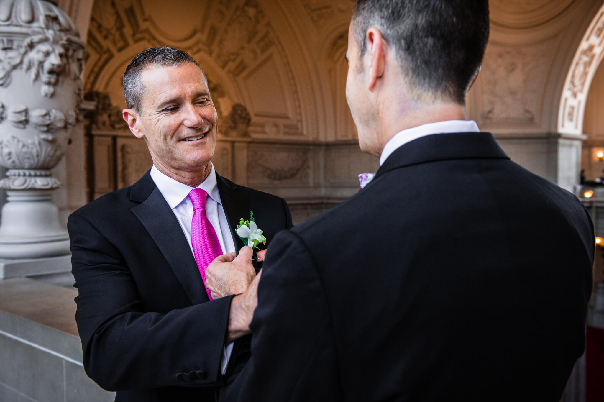 Two men help fasten each other's boutonniere before wedding ceremony