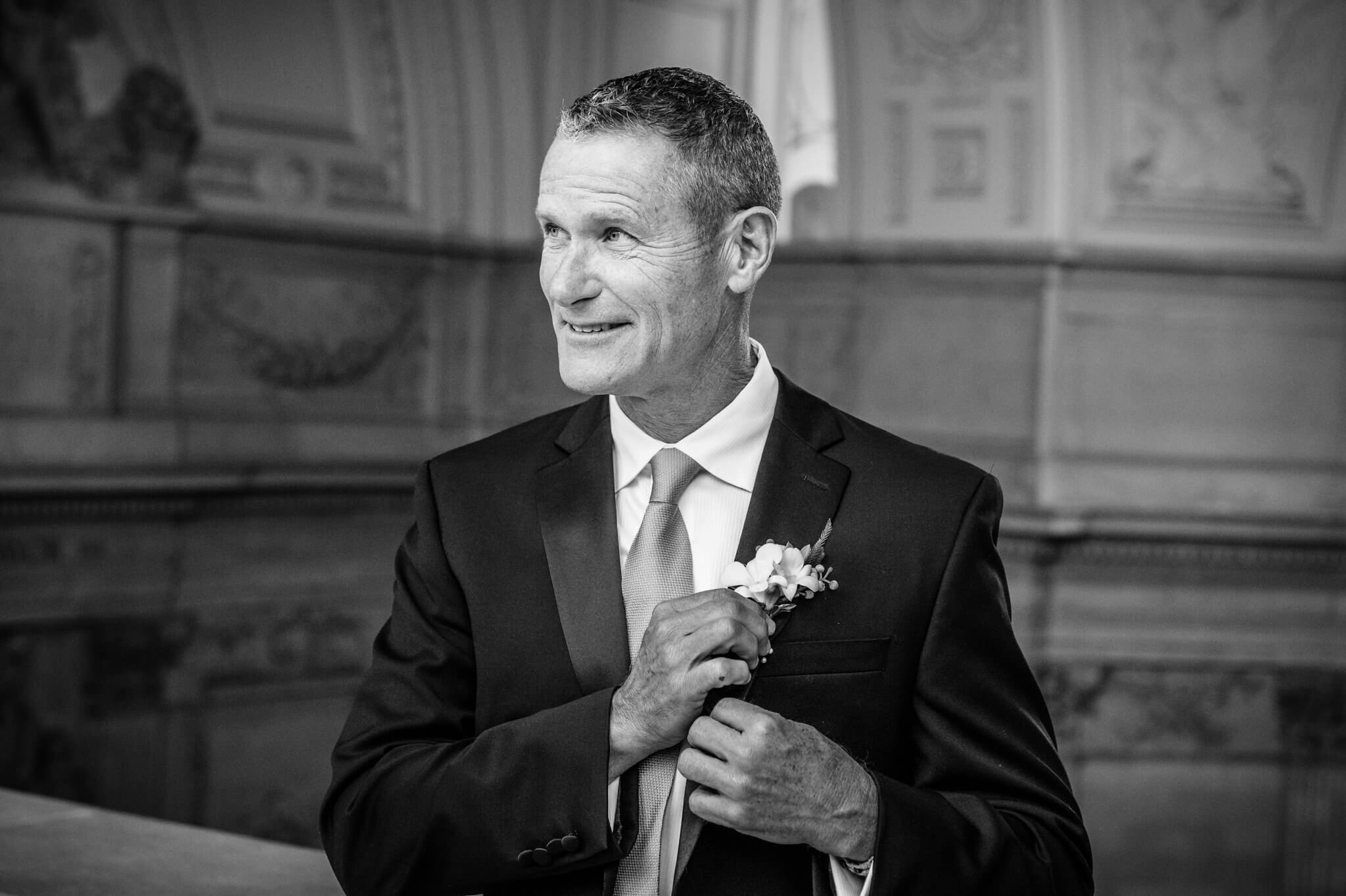 Black and white photo of man smiling and adjusting boutonniere at a wedding