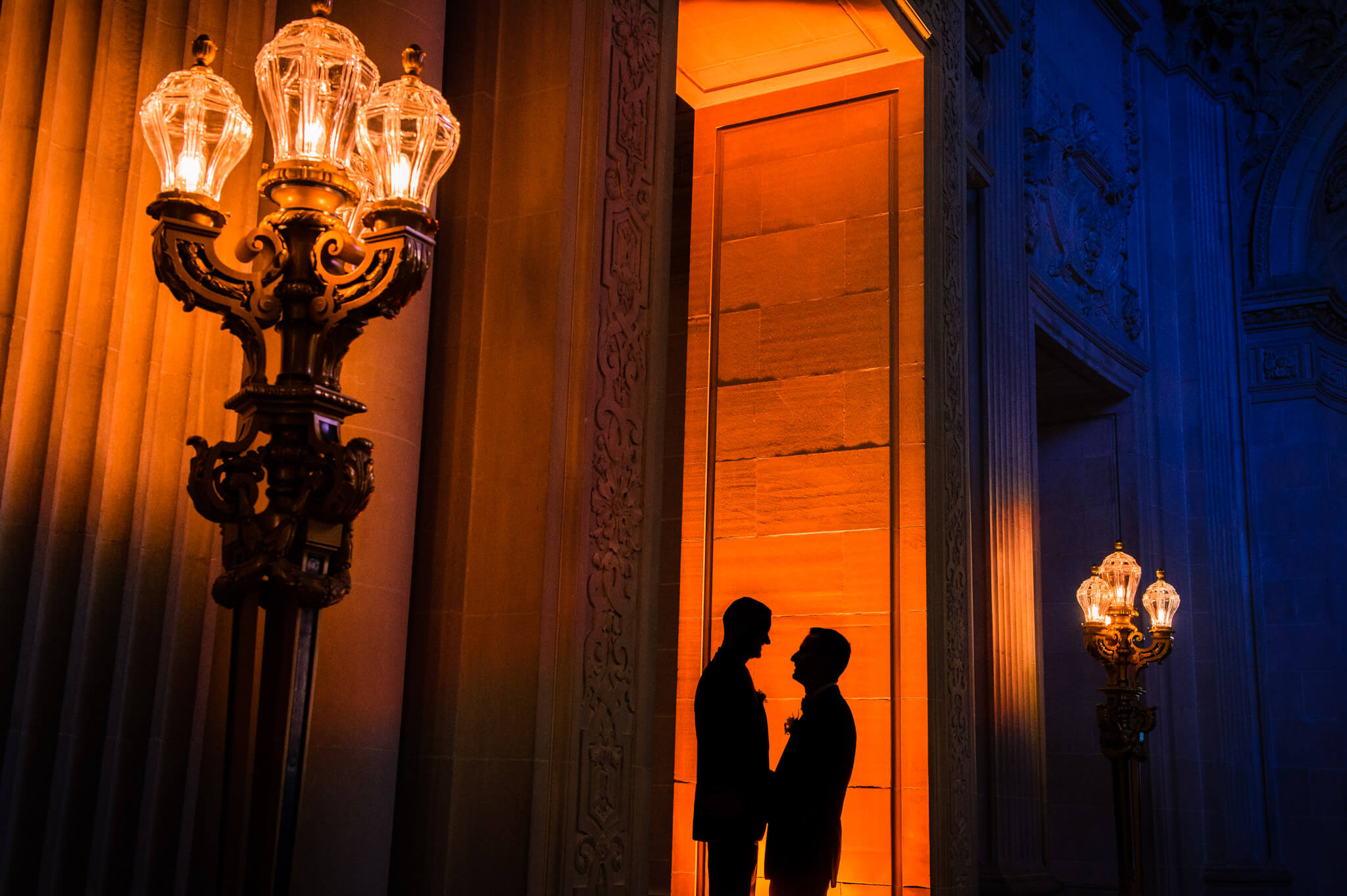 Two newlywed grooms stand together in a large entranceway