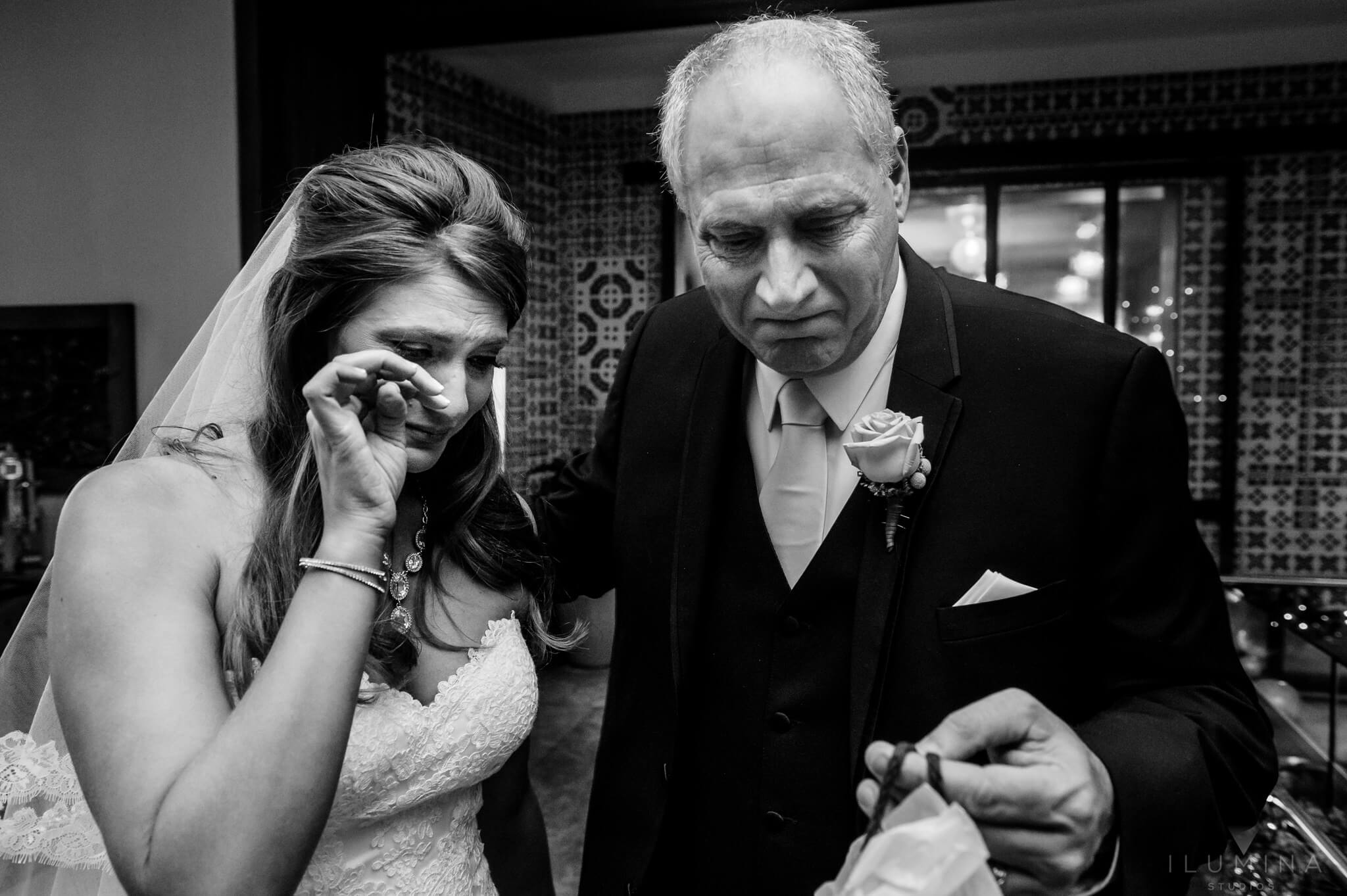 Black and white photo of bride wiping a tear as man next to her picks up gift