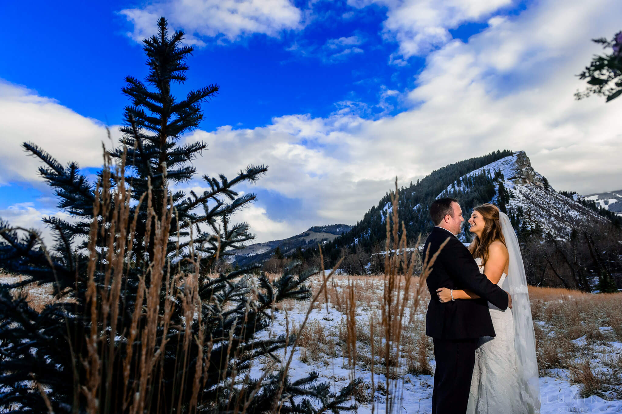Color photo of bride and groom embracing with snowy vail landscape in background