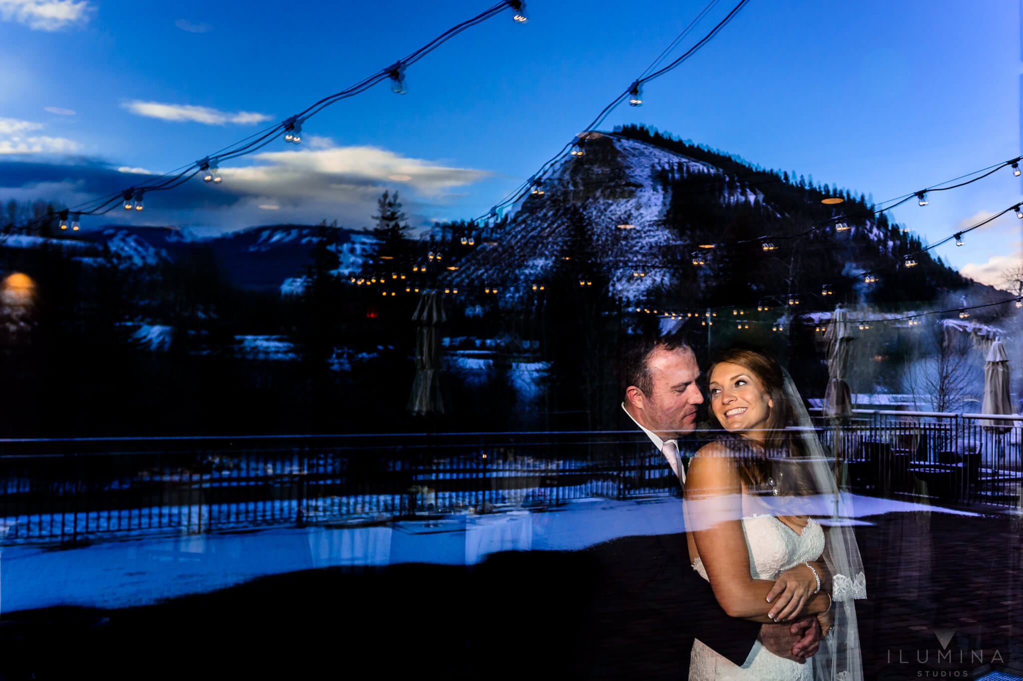 Double exposure color photo of bride and groom embracing and smiling with mountains in background