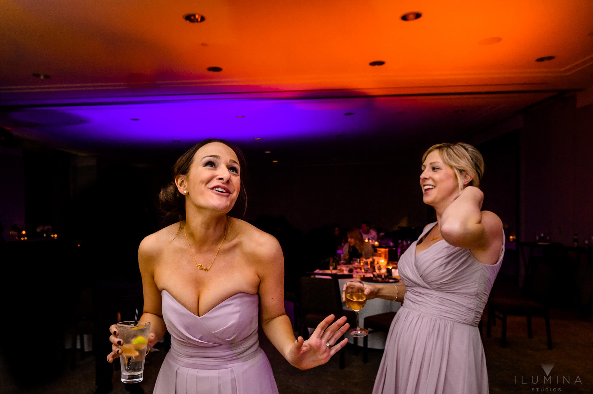 Two bridesmaids in purple dresses laugh and drink at Vail, Colorado wedding