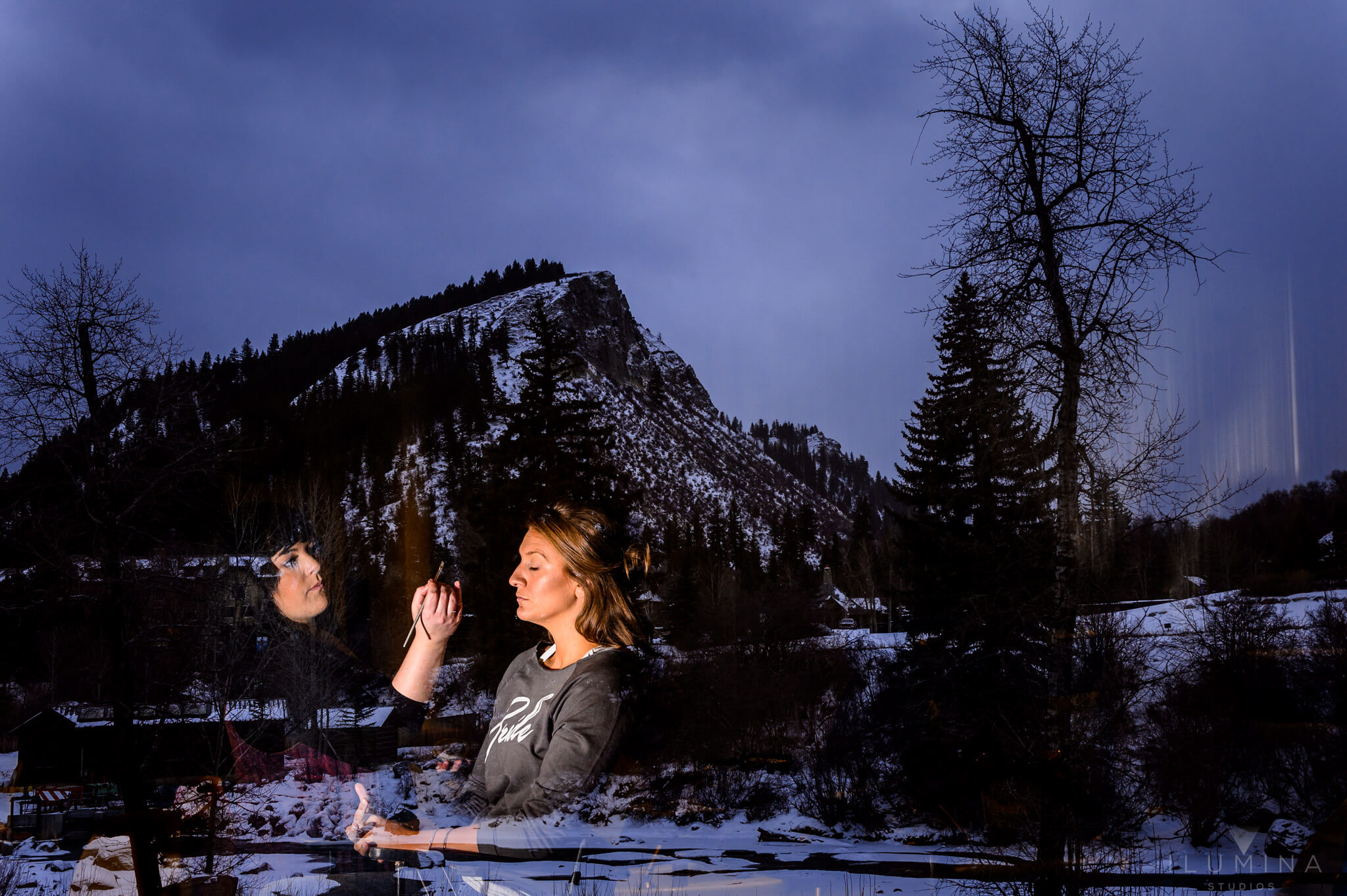 Color double exposure photo of women applying makeup with dusk mountain scene in background