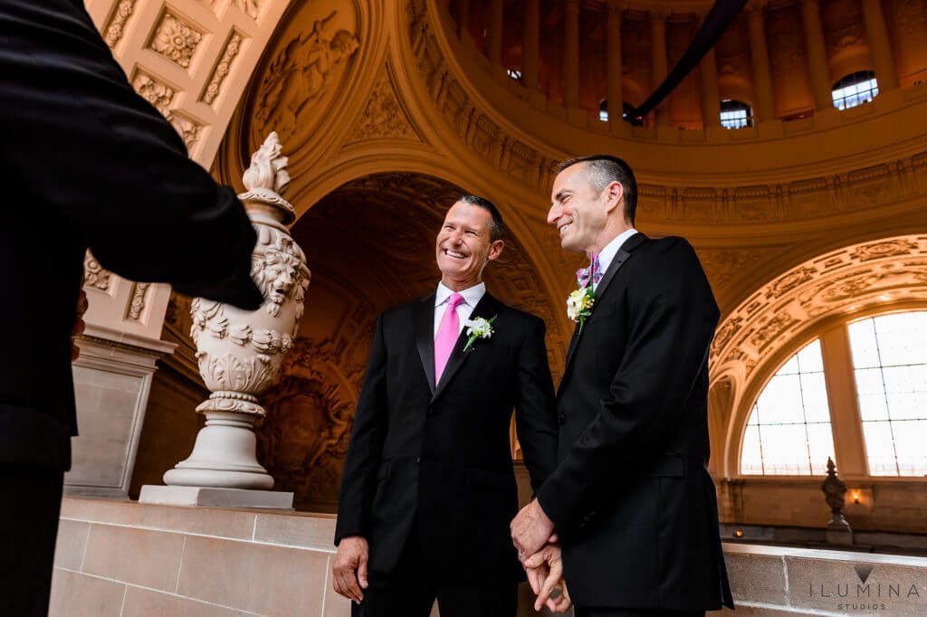 Wedding Photos at San Francisco City Hall. Two men hold hands and laugh at altar during same-sex marriage at the San Francisco City Hall in California