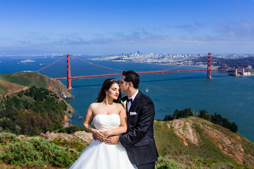 Color landscape wedding photo of groom kissing bride's temple with San Francisco and Golden Gate Bridge in background