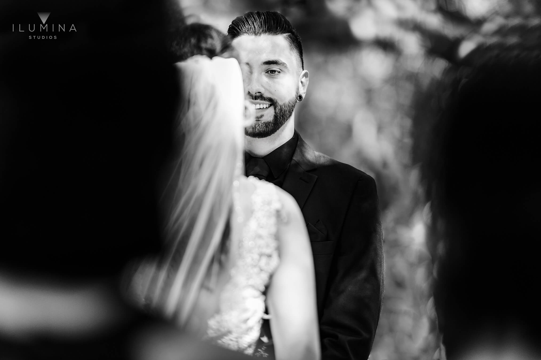Black and white documentary-style wedding photo of groom smiling at bride at Anaheim Oak Canyon Nature Center wedding