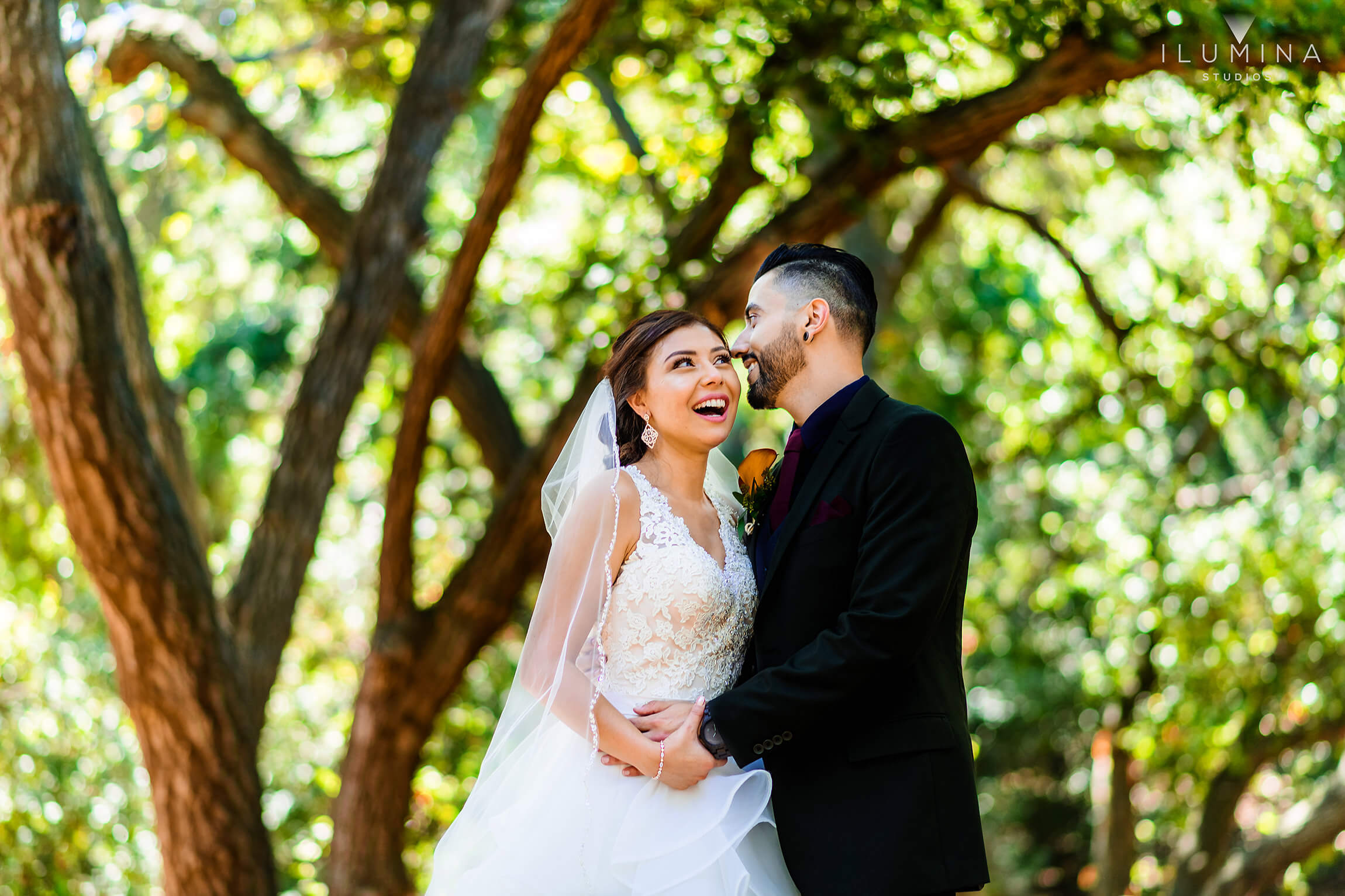 Bride smiles as groom whispers something in her ear with trees in background at Anaheim Oak Canyon Nature Center wedding shoot