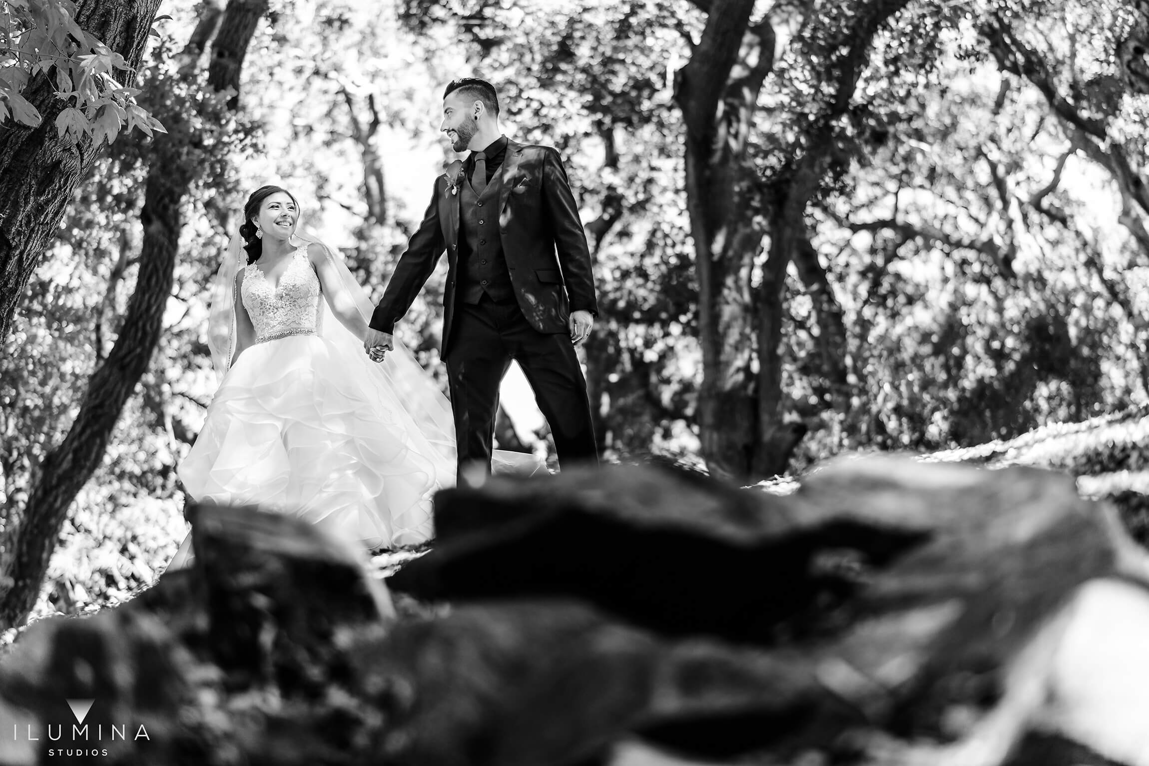 Black and white image of bride and groom holding hands in forest behind rocks at Anaheim Oak Canyon Nature Center wedding shoot