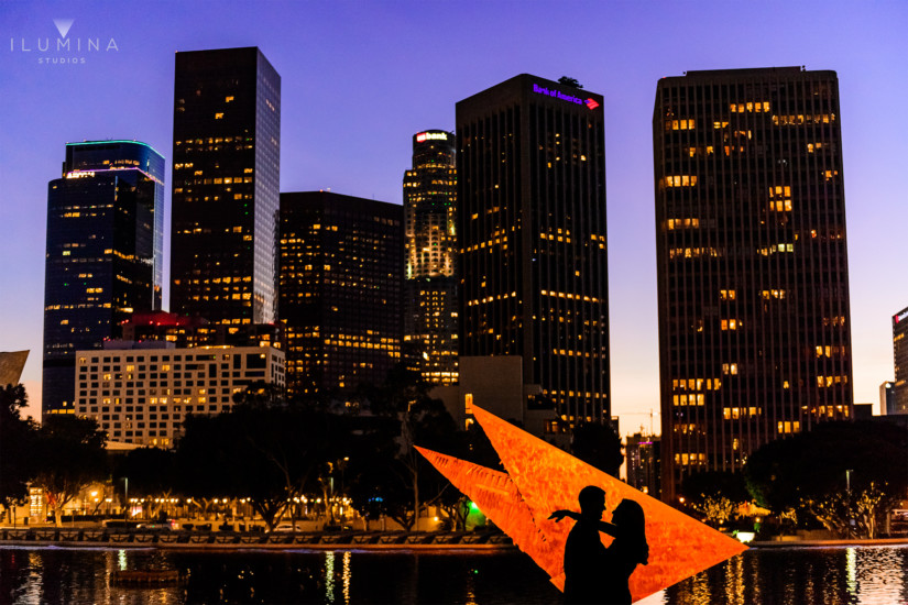 Color engagement photo with silhouette of embracing man and woman projected on orange kites in front of Bank of America during engagement shoot at the Water and Power Building in Los Angeles, California