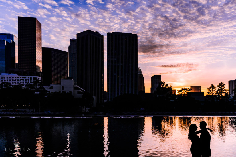 Sunset silhouette engagement photography of man and woman embracing in front of water and cityscape during engagement shoot at the Water and Power Building in Los Angeles, California