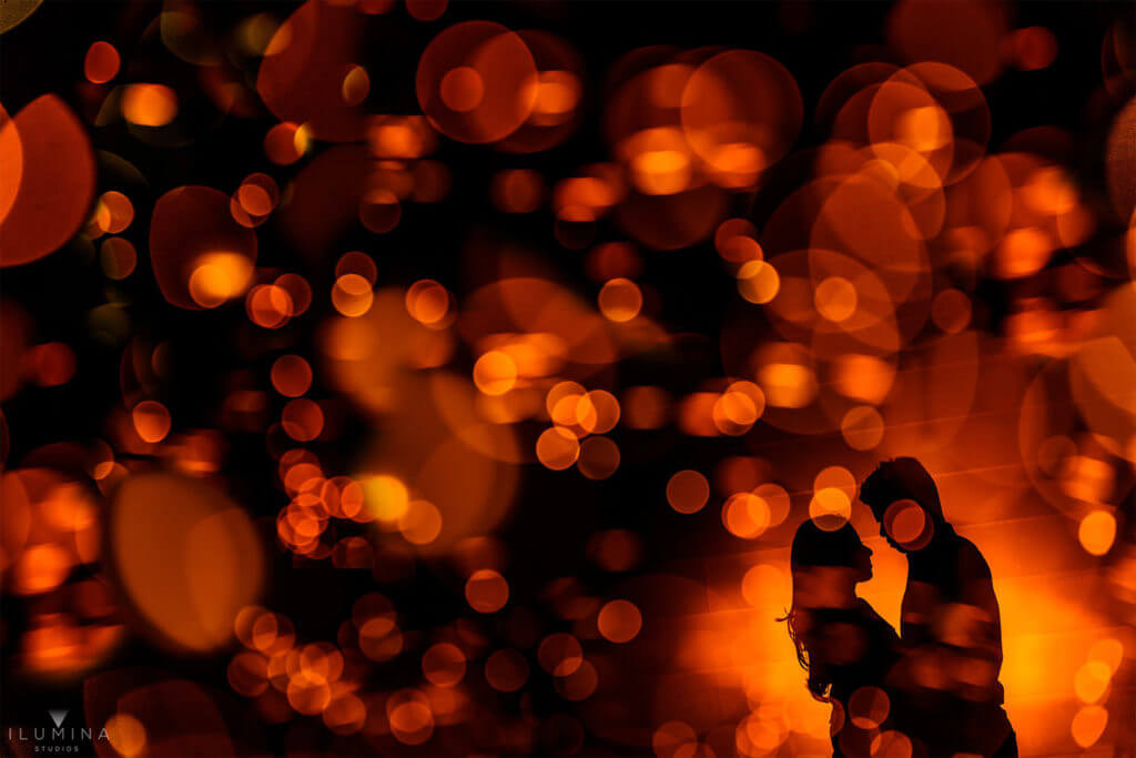 Male and female silhouette embrace each other behind amber bokeh double exposure in Brooklyn, New York