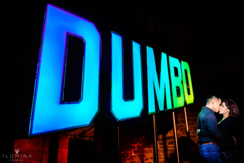 Man and woman kiss in front of blue and green Dumbo sign in Dumbo, Brooklyn, New York