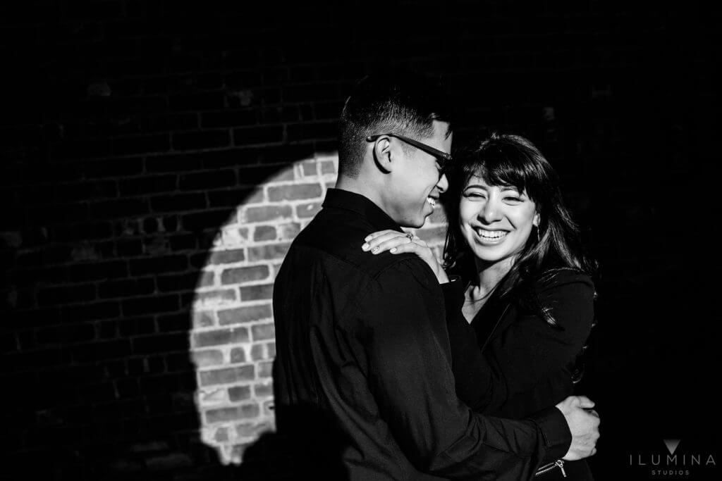 Black and white image of woman smiling at camera while dancing with her fiancé in Brooklyn, New York City