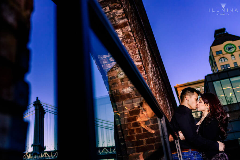 Color photo of man and woman hugging and kissing next to window reflection in Brooklyn, New York City