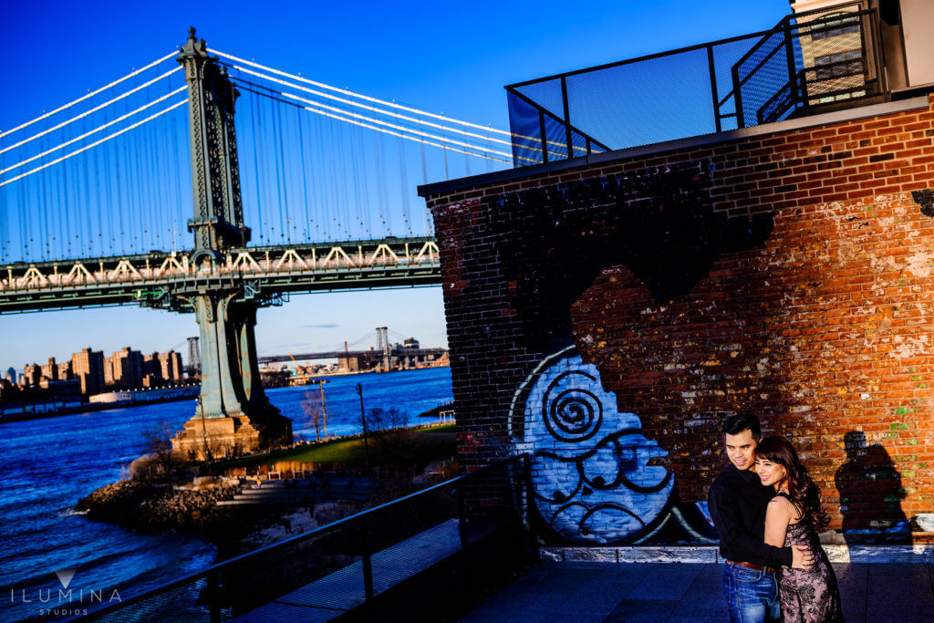 Man and woman hugging in front of brick wall with old graffiti in Brooklyn, New York