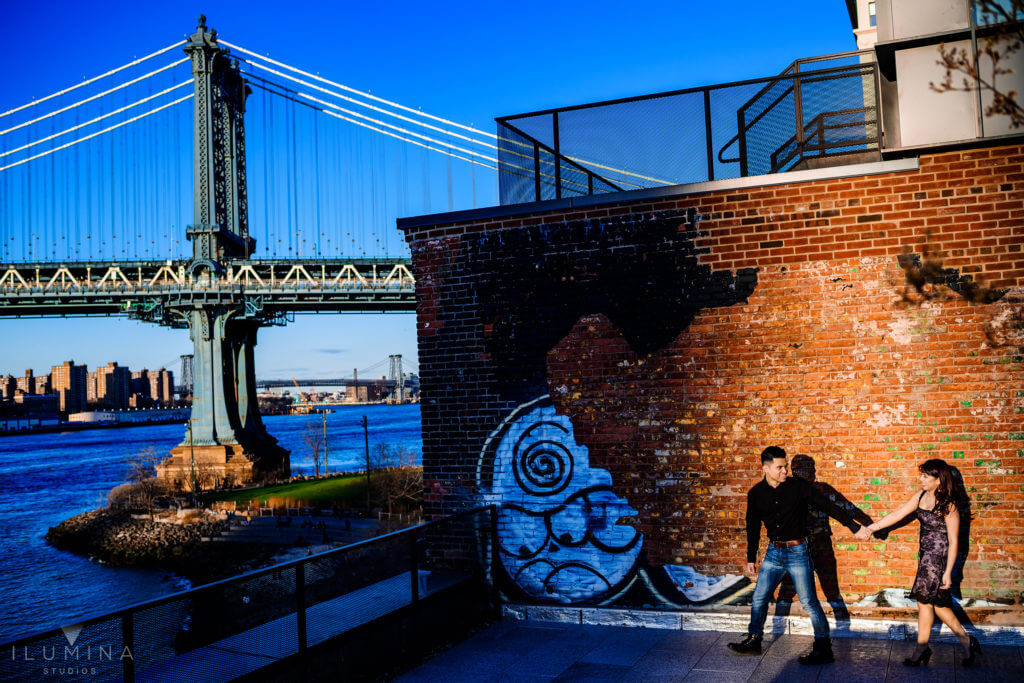 Man leads woman by the hand in front of brick building in Brooklyn, New York