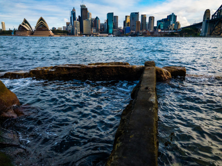 syndey opera house and city in background, closer up are rocks and the water