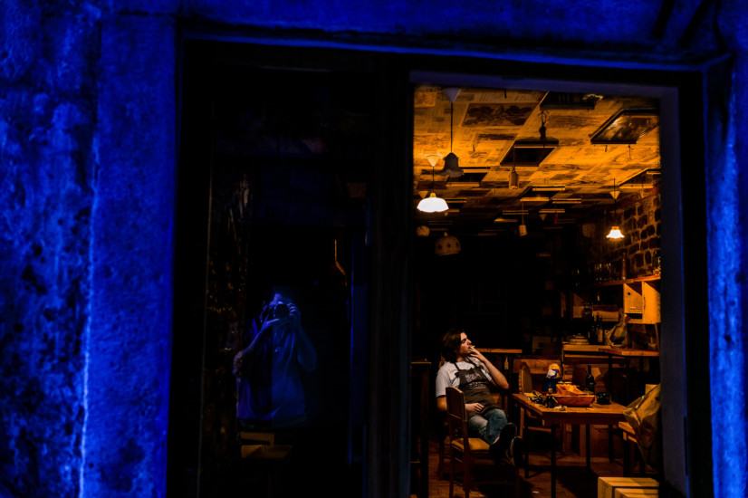 a worker taking a break with a cigarette inside his establishment, reflection of the photographer in window outside