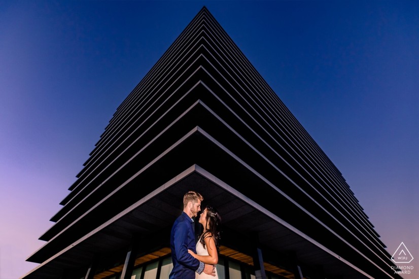 Man and woman embrace near a very sharp cornered abstract building in Los Angeles