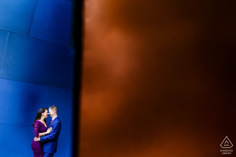 man in blue suit and woman in purple dress holding eachother in front of a blue and golden colored wall