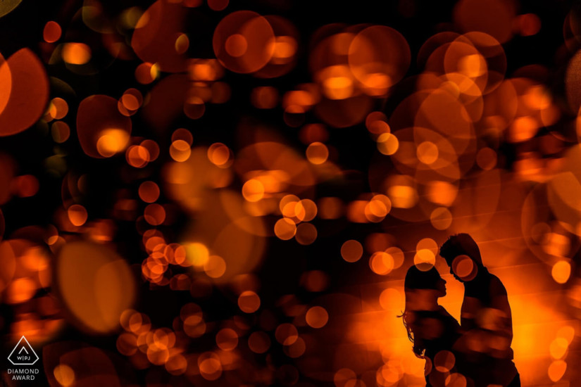 man and woman silhouette holding eachother closely as red and orange colored dots of light rest scattered over the photo